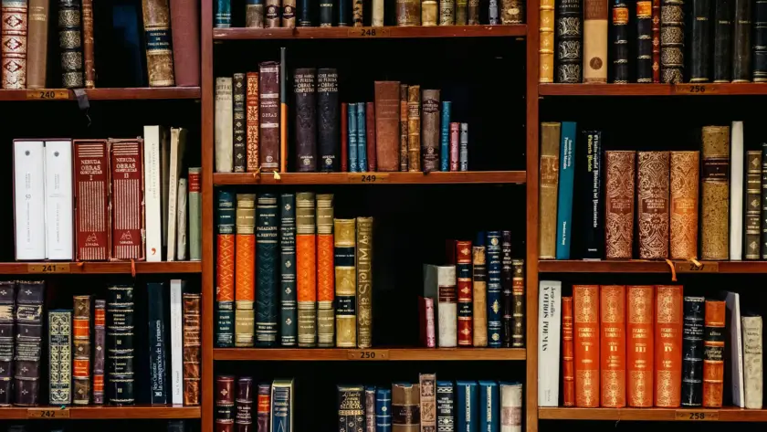 A close-up of a wooden bookshelf filled with various colorful hardback books.