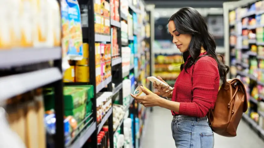 Woman reading a product label in a grocery store aisle.