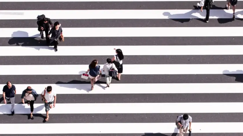 People walking and sitting on a wide striped pedestrian crosswalk.
