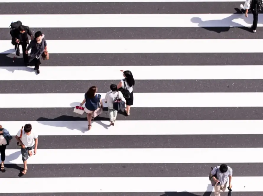 People walking and sitting on a wide striped pedestrian crosswalk.