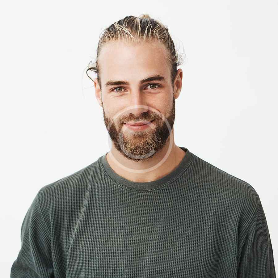Smiling man with braided hair and beard wearing a gray sweater.
