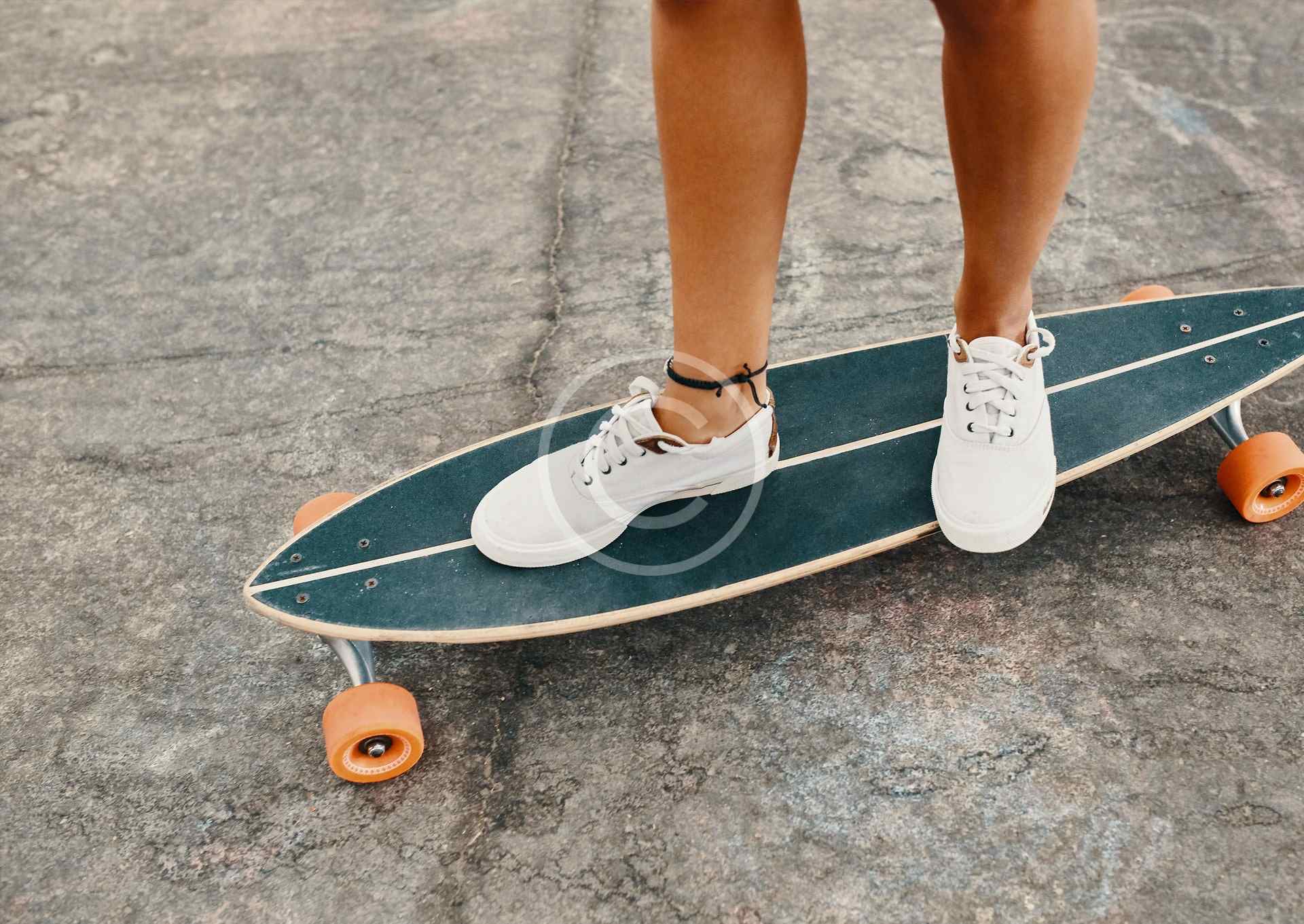 Person riding a skateboard on a paved surface wearing white sneakers.