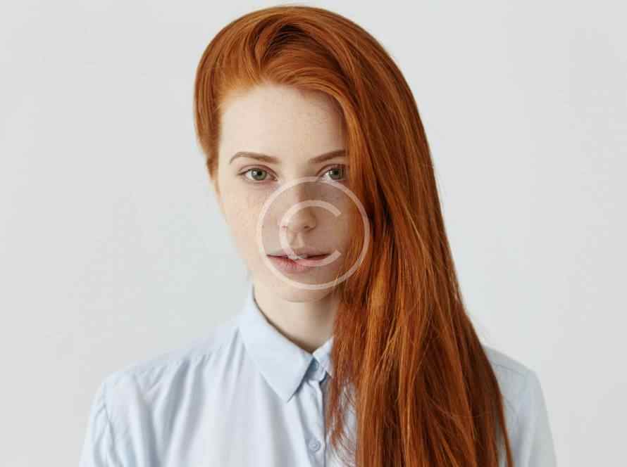 Portrait of a red-haired woman with glasses and a light blue shirt.