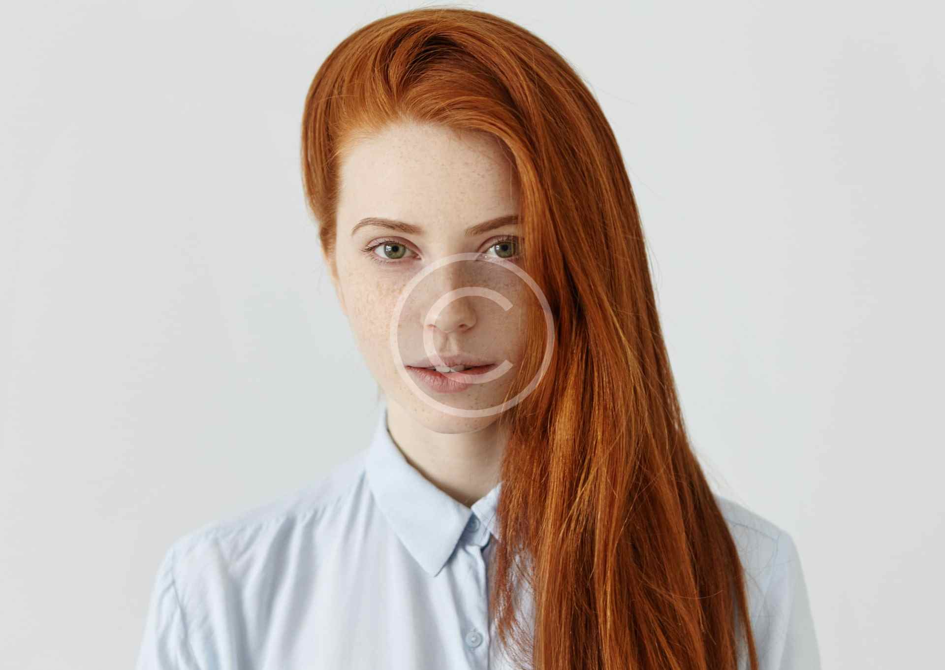 Portrait of a red-haired woman with glasses and a light blue shirt.