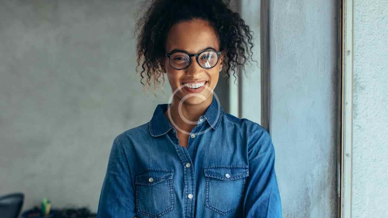 Confident young woman with glasses and curly hair smiling indoors.
