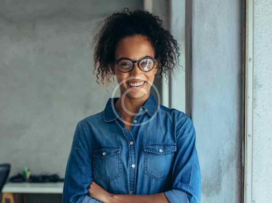 Confident young woman with glasses and curly hair smiling indoors.