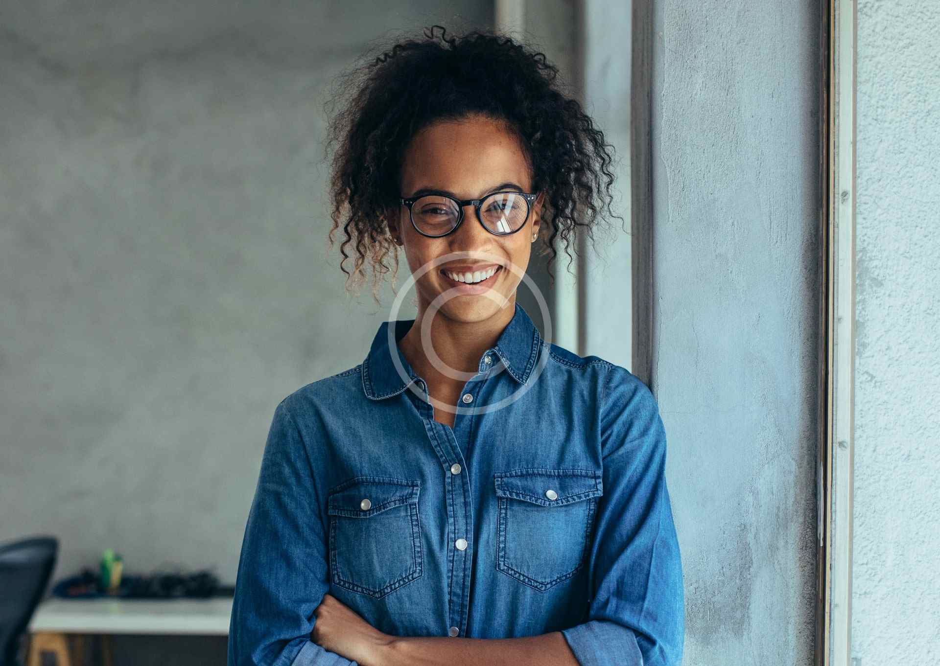 Confident young woman with glasses and curly hair smiling indoors.