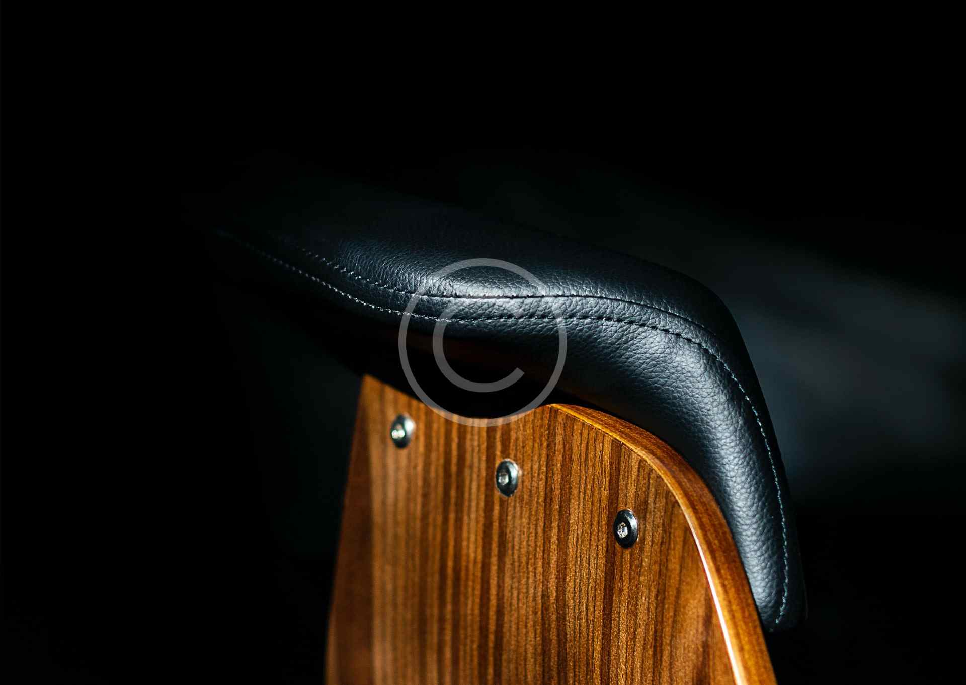 Close-up of a wooden chair with black leather upholstery and metal studs.