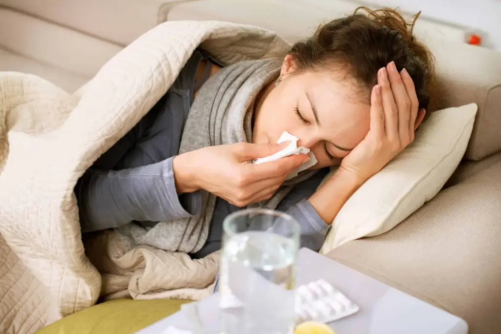 Woman lying in bed, blowing her nose with a tissue.