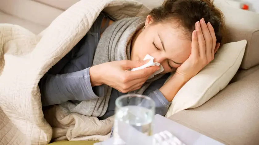 Woman lying in bed, blowing her nose with a tissue.