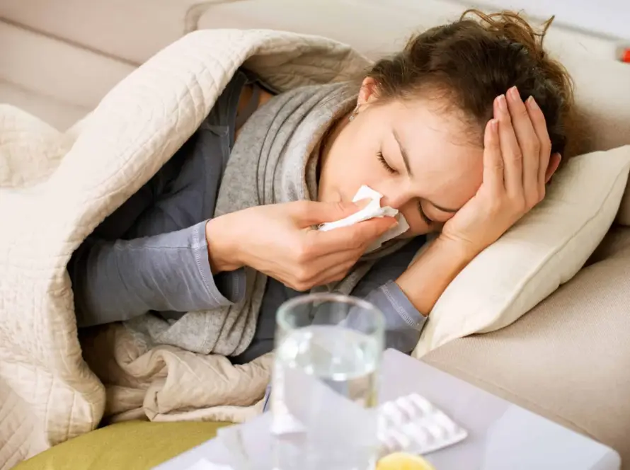Woman lying in bed, blowing her nose with a tissue.