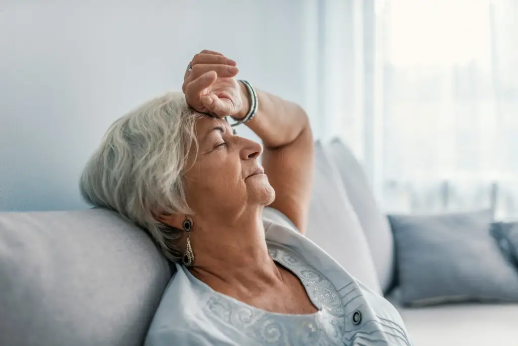 An elderly woman resting with a hand on her forehead, looking thoughtful.