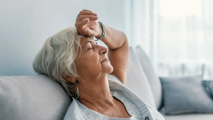 An elderly woman resting with a hand on her forehead, looking thoughtful.
