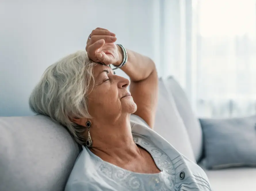 An elderly woman resting with a hand on her forehead, looking thoughtful.