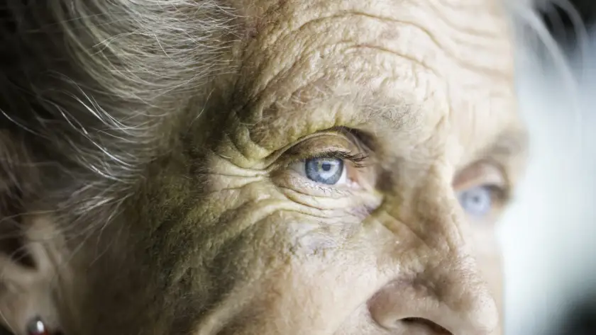Close-up of an elderly person's face with blue eyes and wrinkles.
