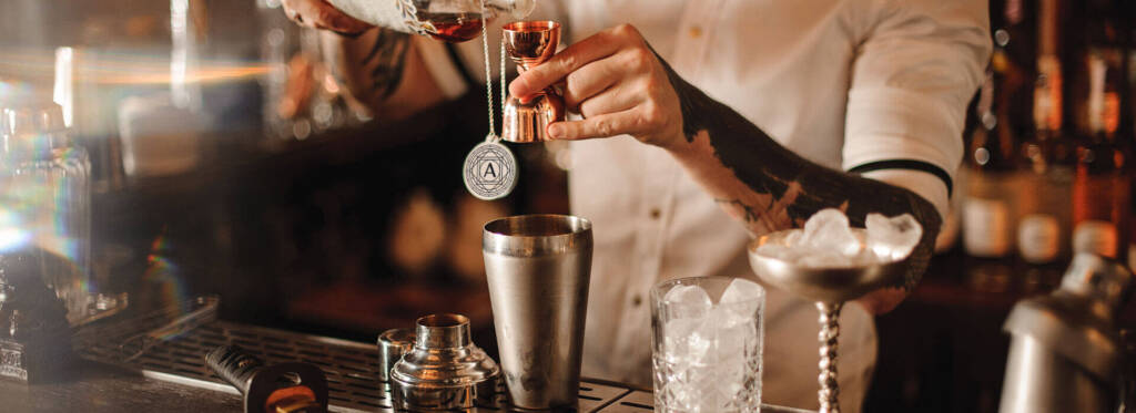 Bartender pouring a spirit into a cocktail shaker.