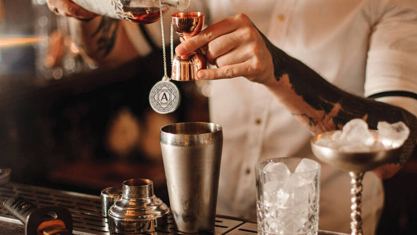 Bartender pouring a spirit into a cocktail shaker.