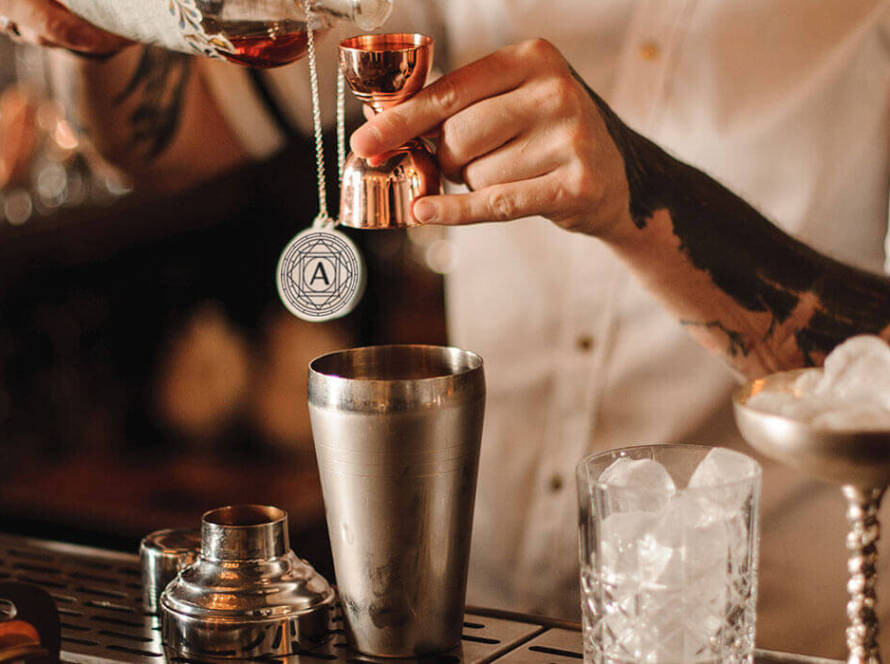 Bartender pouring a spirit into a cocktail shaker.