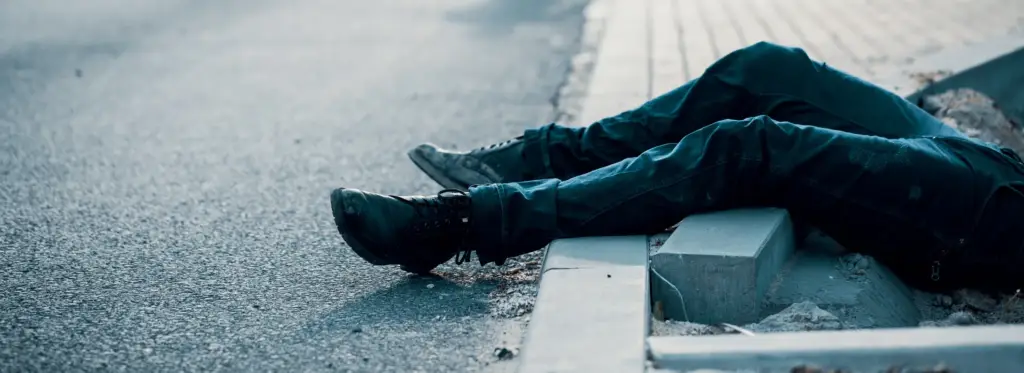 Person sitting on a curb with legs stretched out on the road.