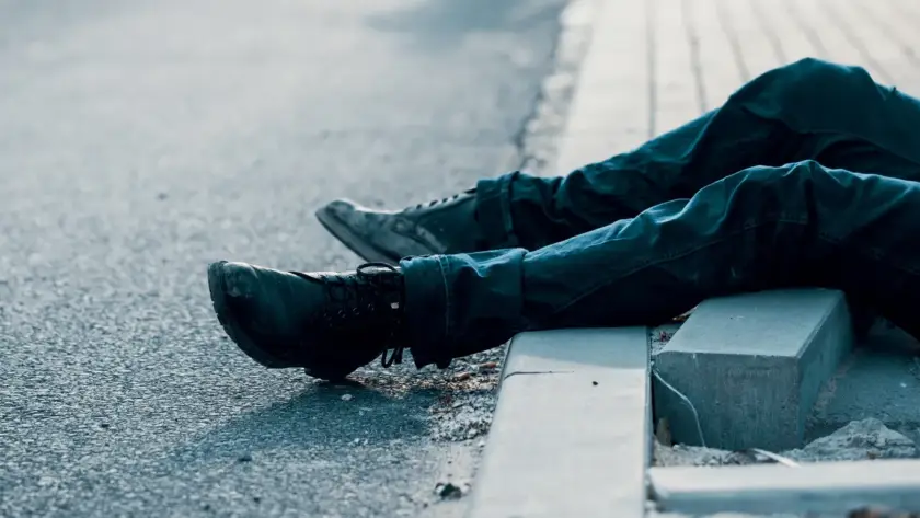 Person sitting on a curb with legs stretched out on the road.