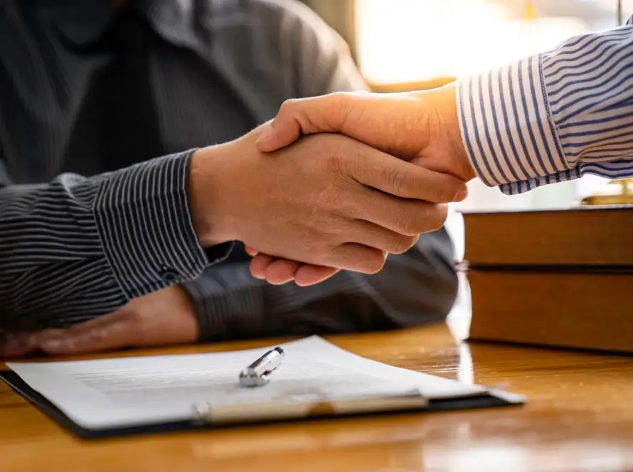 Two people shaking hands over a contract on a table.