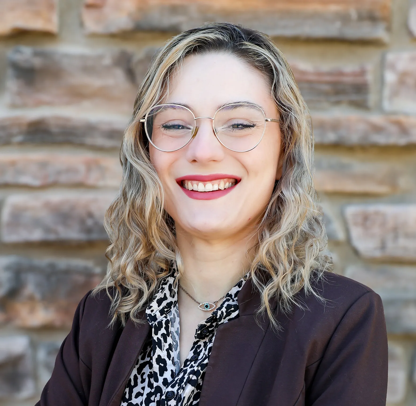Smiling woman with glasses and curly hair in a professional outfit.