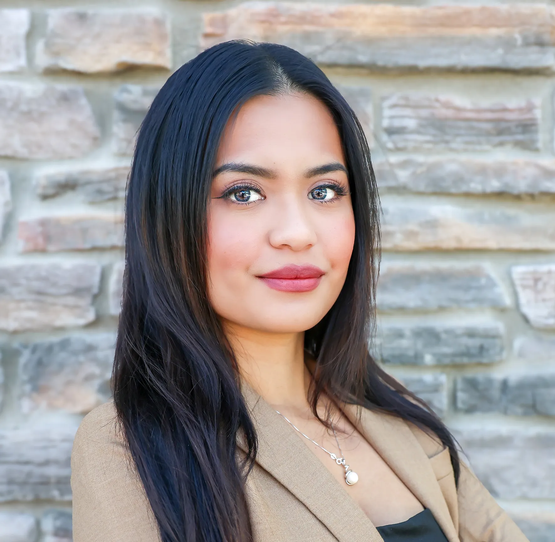 Portrait of a confident woman with long black hair against a stone wall.