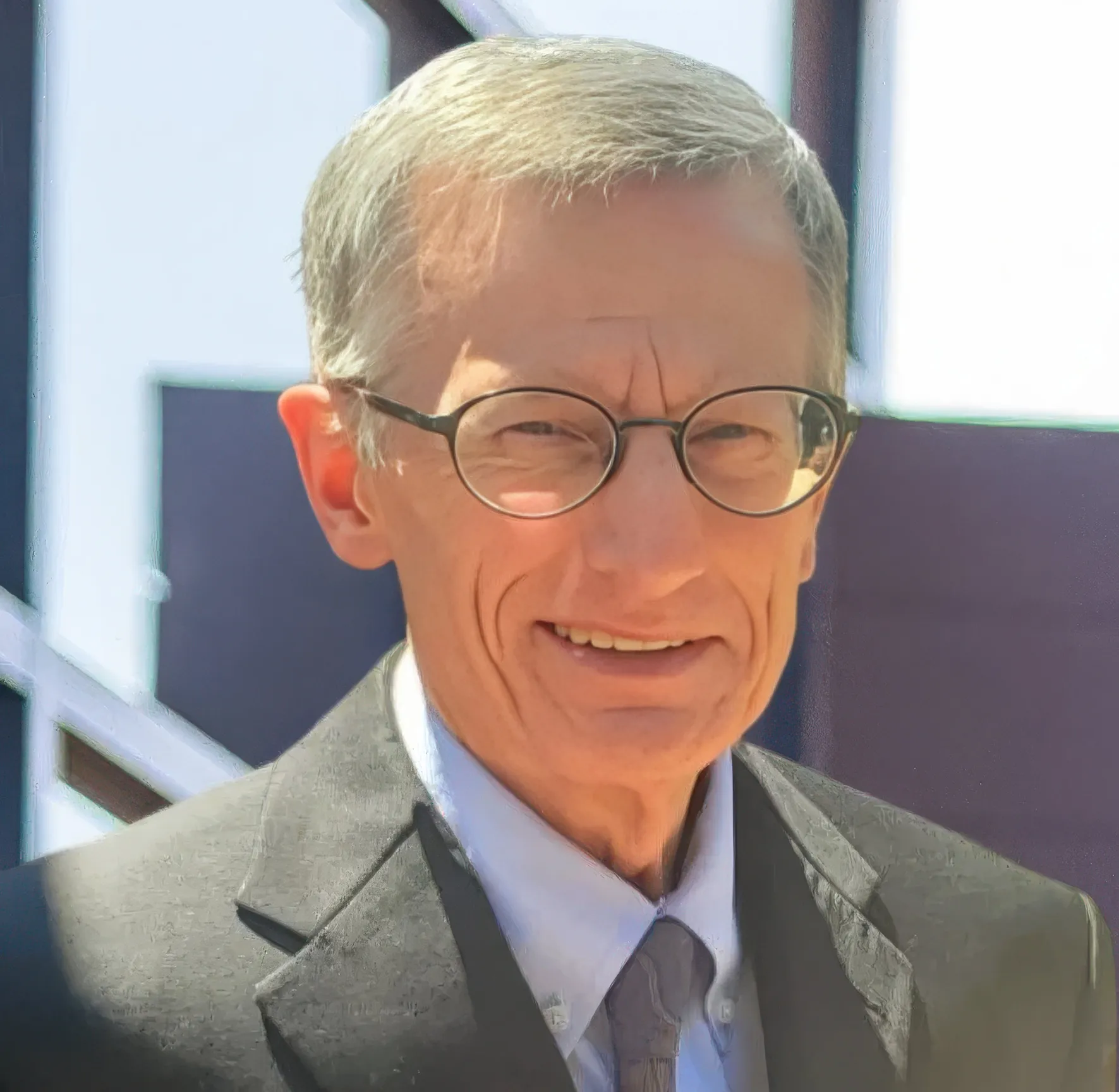 Older man with glasses in a suit smiling indoors.