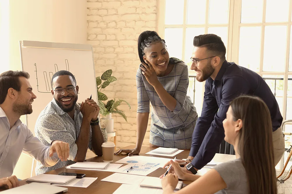 A diverse team collaborating and smiling around a table with documents.
