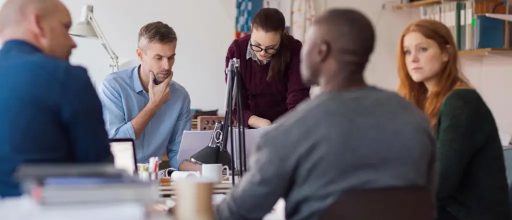 People collaborating around a table with microphones and laptops.