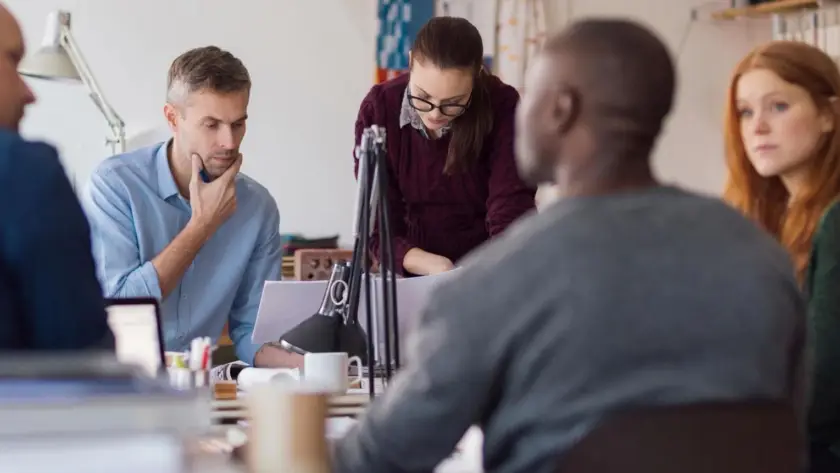 People collaborating around a table with microphones and laptops.