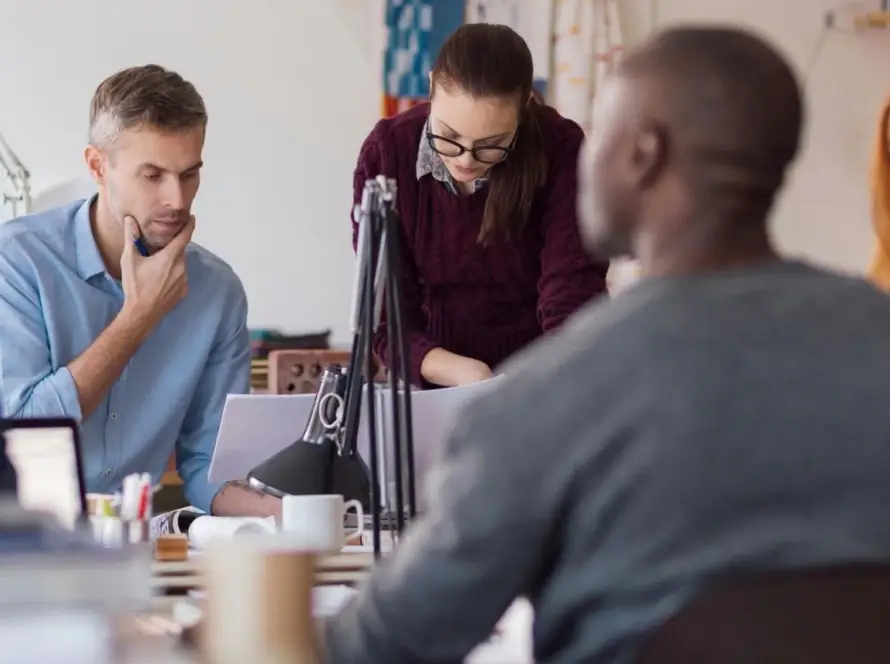 People collaborating around a table with microphones and laptops.