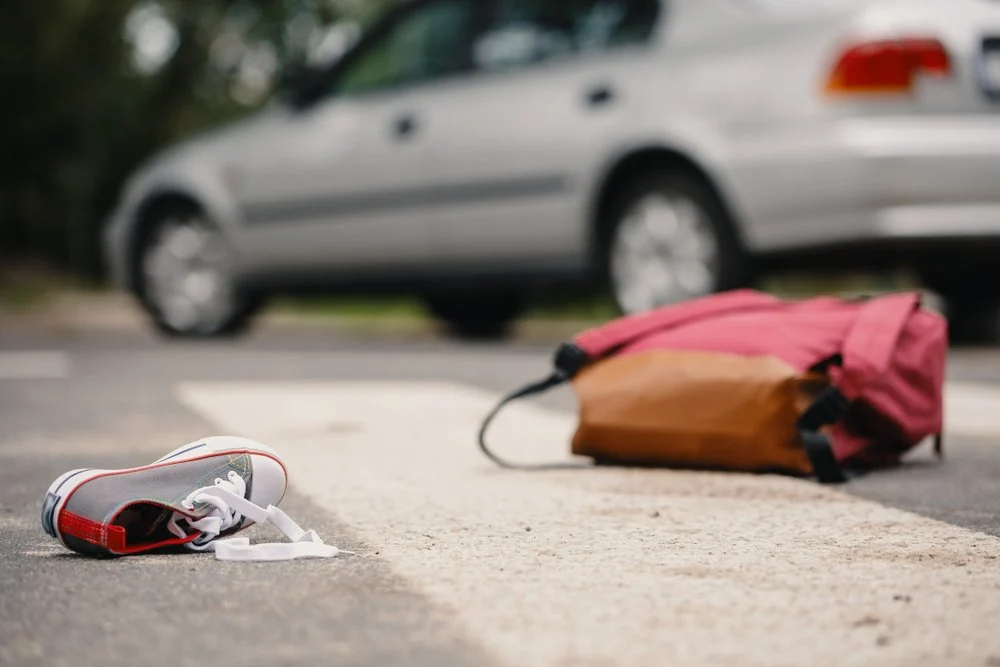 Discarded face mask and bag on a sidewalk with a parked car in the background.