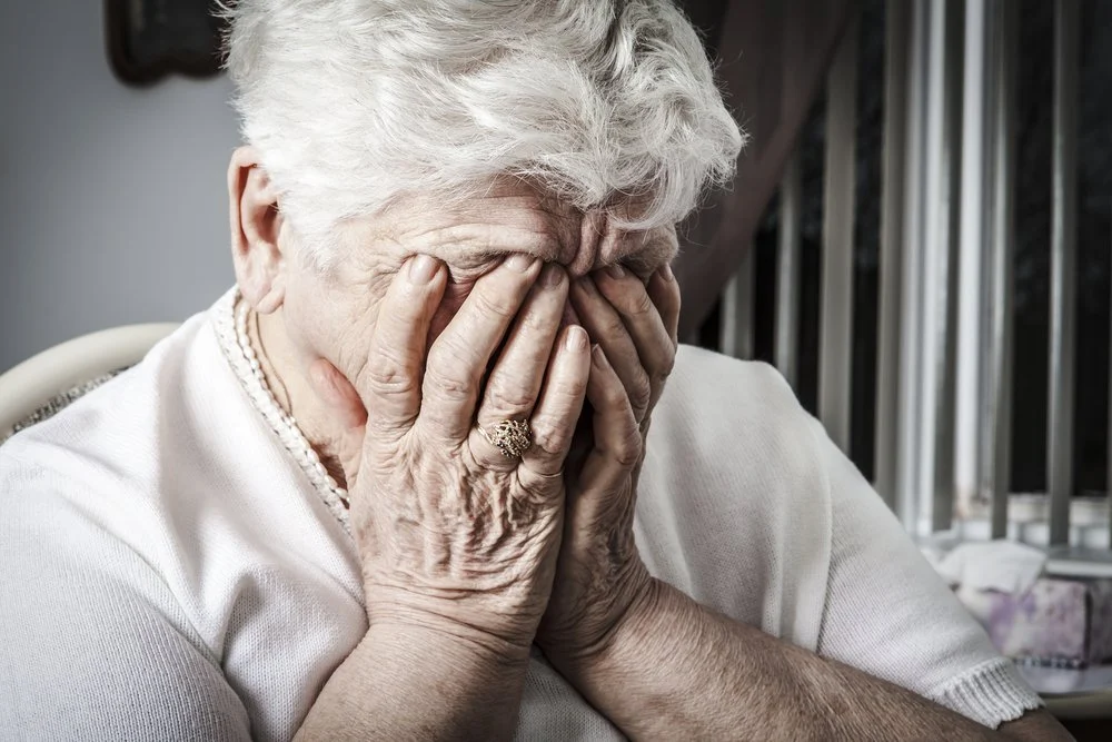 Elderly woman covering her face, expressing distress.