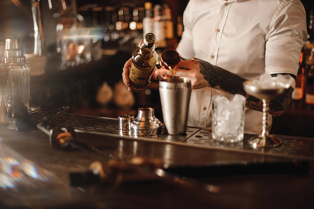 Bartender garnishing a cocktail with herbs at a bar.