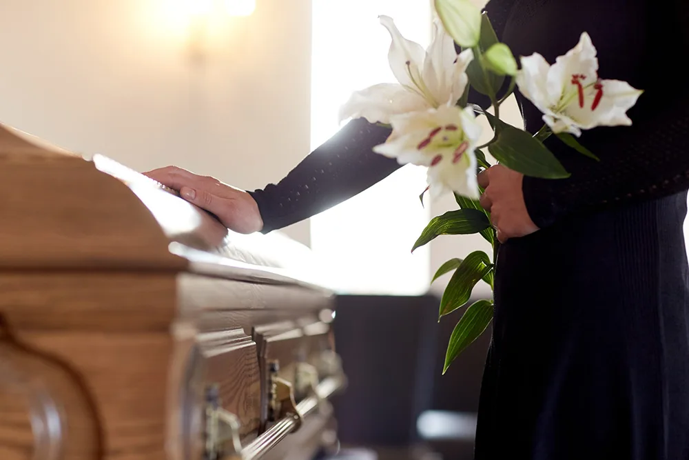 Person mourning beside a coffin with white lilies.