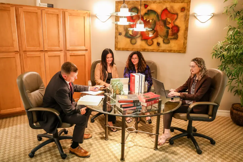 Four people engaged in a lively discussion around a glass table in a warmly decorated room.